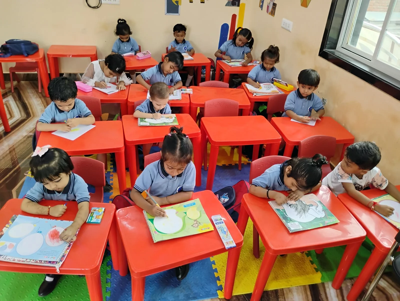 Children working on activity sheets at red classroom desks
