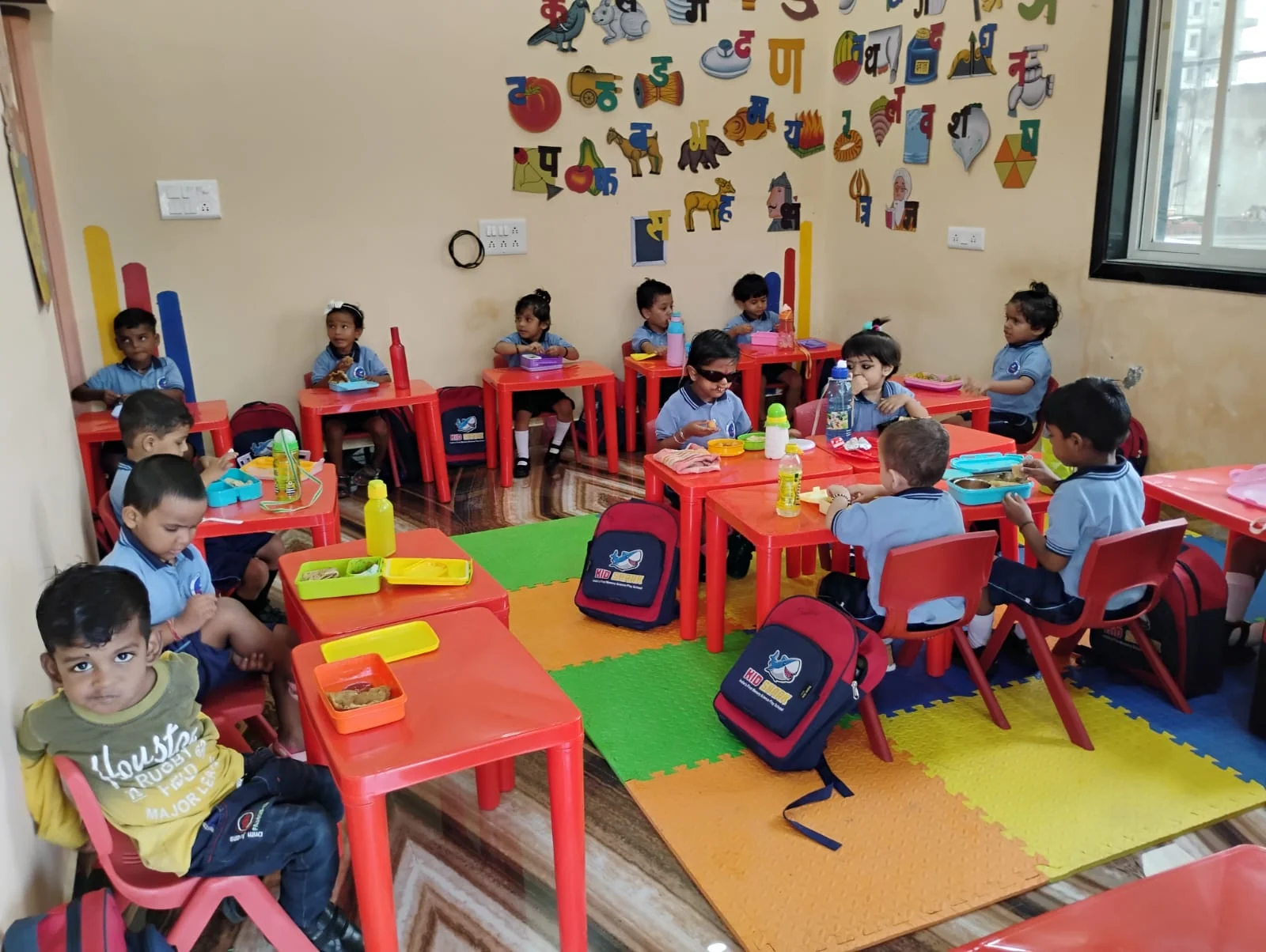 Children seated around red desks in the school classroom