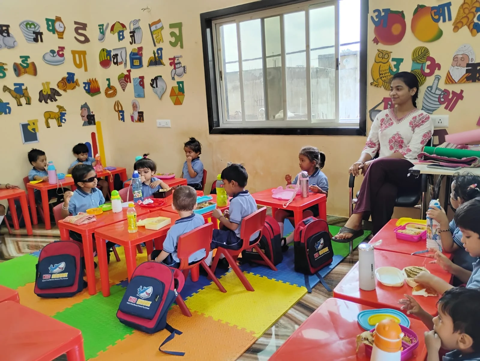 A teacher alongside children seated in the colourful classroom